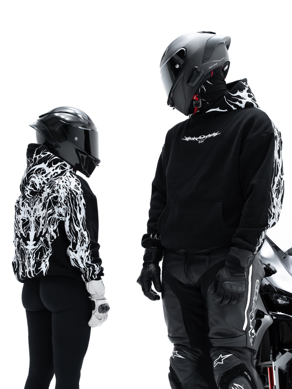 Two models wearing black Alpinestars motorcycle apparel with white flame-patterned sleeves and hood, complete with helmets and riding pants, set against a solid white background.
